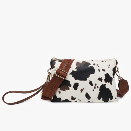 Cow print handbag with brown strap on a white background