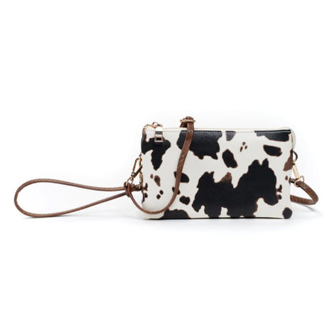 Cow print handbag with brown strap on a white background