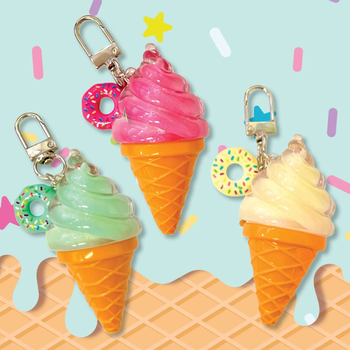 Three ice cream cone keychains with silver clasps, featuring pink, mint green, and pale yellow swirls in waffle cones with colorful sprinkle donut charms, set against a light blue background with pastel confetti and waffle graphics.