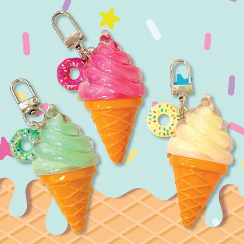 Three ice cream cone keychains with silver clasps, featuring pink, mint green, and pale yellow swirls in waffle cones with colorful sprinkle donut charms, set against a light blue background with pastel confetti and waffle graphics.