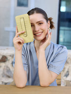 Woman holding a yellow wallet in front of her face, smiling.